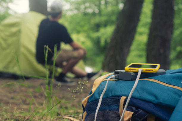 智能手机使用便携式充电器充电。Power Bank在户外用背包给手机充电，背景是一个帐篷和一名游客。图片下载