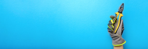 钳。一个电工手里拿着黄色和黑色的钳子，上面是蓝色的单色背景。维修和安装工具。横幅的设计和印刷施工主题。图片下载