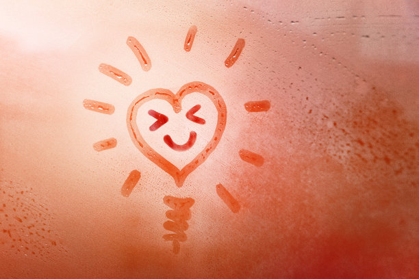 手画橘形心像太阳，微笑着幸福的脸眯着眼睛和灯在泥泞的玻璃潮湿的橙色窗户在城市日落图片下载