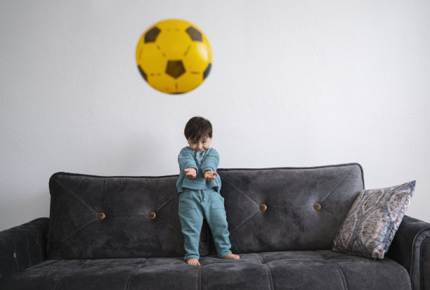 可爱的小男孩在客厅的沙发上踢足球图片下载