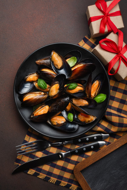 海鲜贻贝和罗勒叶在一个黑色的盘子，叉子，刀和礼品盒在毛巾和生锈的背景图片下载