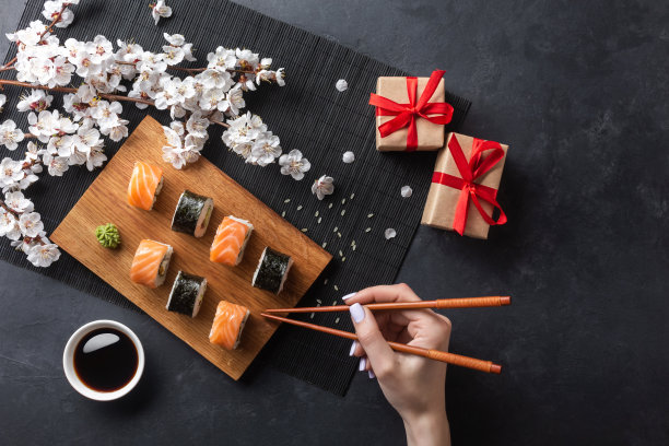 一套寿司和寿司卷，手拿筷子，礼盒和白花枝在石头桌上图片下载
