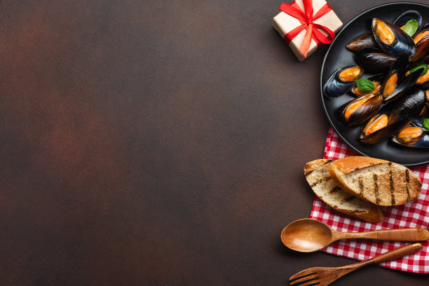 海鲜贻贝和罗勒叶在一个黑色的盘子，毛巾，面包片，木勺和叉子生锈的背景图片下载
