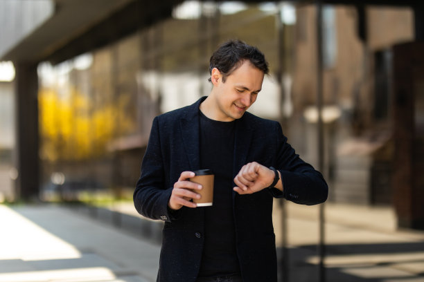 工作的时候了。商人看智能手表和拿着杯子在户外图片下载