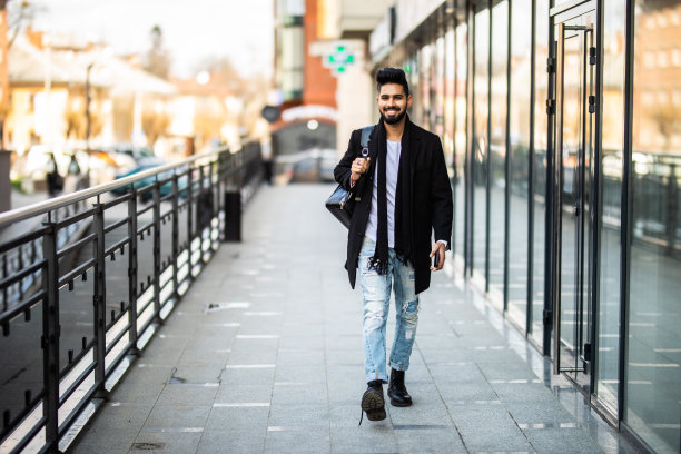 一个时髦的年轻人背着背包走在城市的街道上。图片下载
