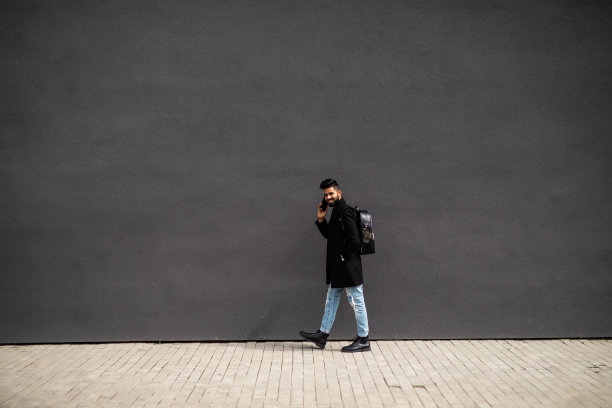 年轻人在灰色背景墙上的街上讲电话。生活方式,技术。图片下载