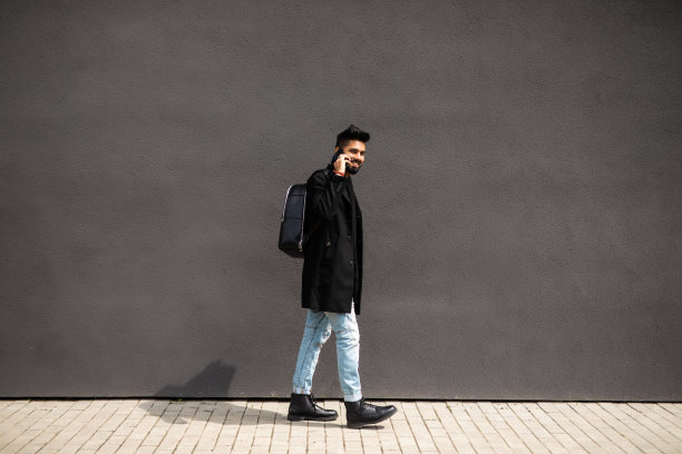 年轻人在灰色背景墙上的街上讲电话。生活方式,技术。图片下载