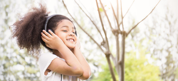 可爱的小女孩在公园里听音乐跳舞的肖像。绿色春夏季教育音乐疗法放松时间概念横幅(模糊)图片下载
