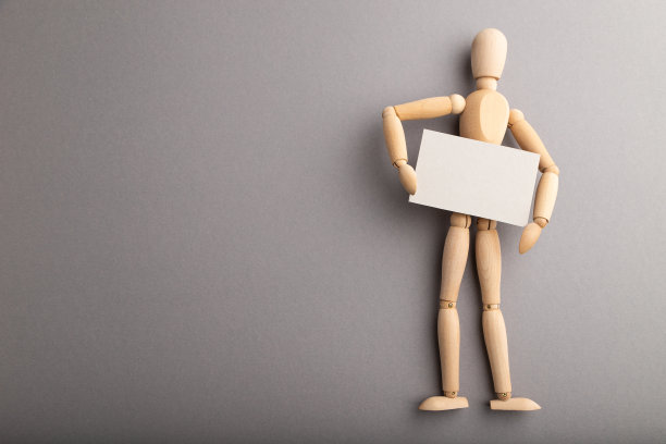 木制人体模型抱着空白海报在灰色柔和的背景。拷贝空间，隔离，表示概念。图片下载