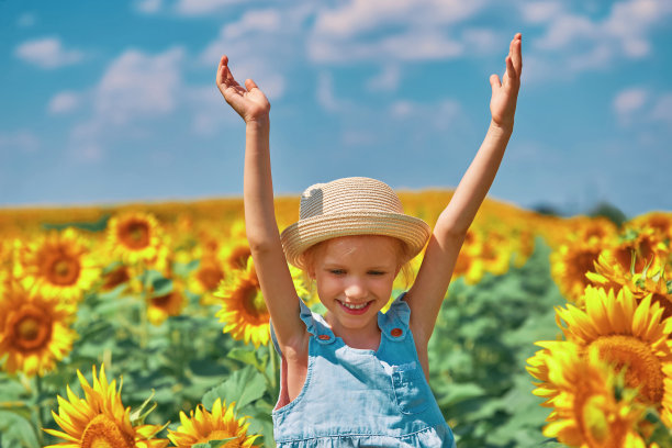 快乐的孩子女孩在帽子有乐趣在田野盛开的向日葵对蓝天的背景。自由的概念图片下载