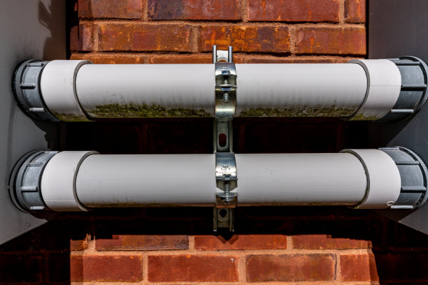 在商业建筑外的砖墙上安装的两块电板之间的塑料管道。图片下载