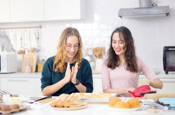 美丽的面包师做糕点，可爱的快乐的两个女人有乐趣的面包制作教室，用他们的手拍面团在一起做蛋糕在家庭厨房。图片下载