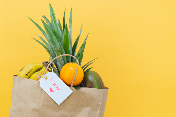 纸购物袋与热带水果和标签与字当地在黄色背景。副本的空间。图片下载