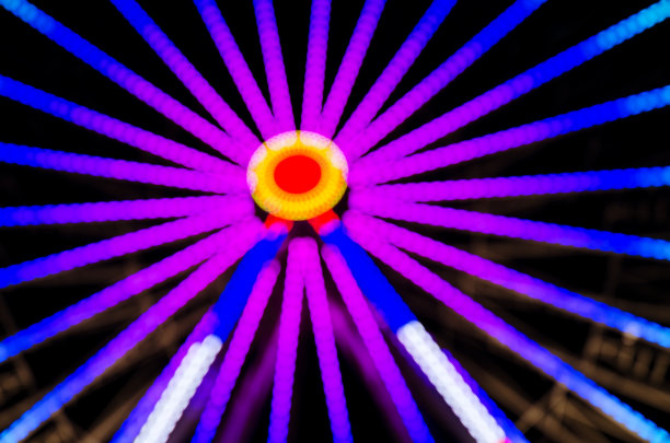 游乐园晚上的图像散焦和模糊。夜景下的摩天轮和云霄飞车。公园骑图片下载