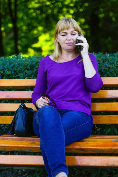 把白种金发女人的镜头移开，在外面打电话，在外面。一个穿着紫色上衣的40多岁女人。成年人使用电话。垂直的。的焦点图片下载