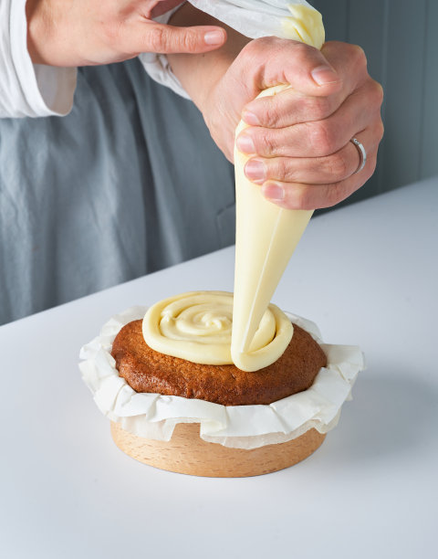 女厨师用糕点包用奶油装饰刚烤好的蛋糕。特写照片，复制空间。自制糕点的概念，烹饪蛋糕。图片下载