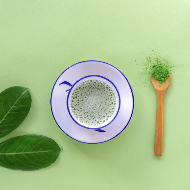 绿茶抹茶放在白色杯子里，茶粉放在木勺里，俯视图。健康的饮料。平躺图片下载