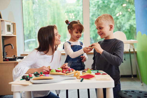 年轻女子带着小男孩和小女孩一起在厨房里玩玩具图片下载