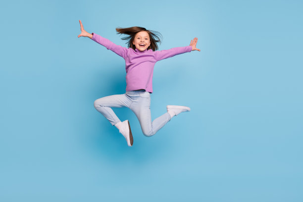 可爱有趣的小女生穿着紫色高领微笑跳高孤立的蓝色背景的照片图片下载