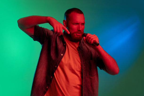 工作室图像的年轻白种人与麦克风隔离在梯度绿色蓝色背景霓虹灯。图片下载