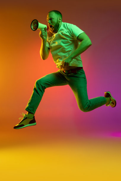 全尺寸的肖像，年轻的白人男子跳跃与扩音器隔离在梯度橙色粉色背景霓虹灯。图片下载