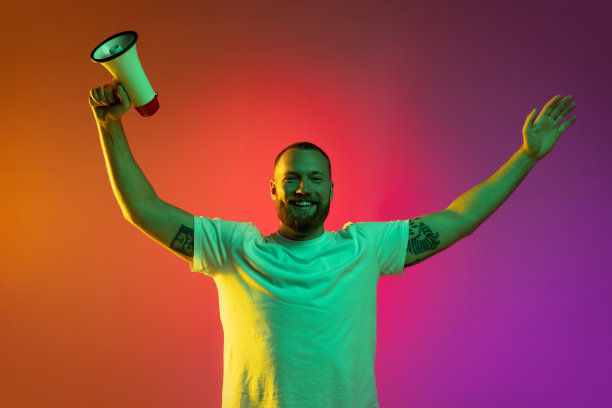 一个高举着扩音器的年轻白人男子的肖像，在霓虹灯的橙色背景下被隔离开来。图片下载