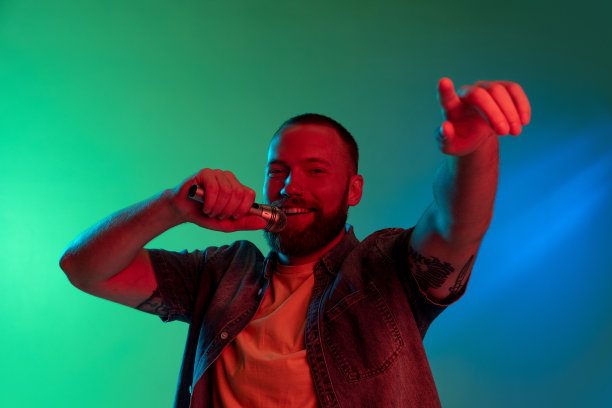 说话或唱歌。工作室图像的年轻白种人与麦克风隔离在梯度背景霓虹灯。图片下载