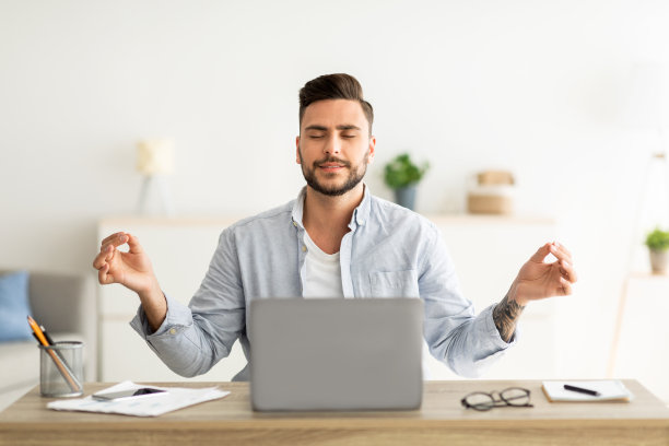 保持冷静。男性自由职业者一边在笔记本电脑上工作一边沉思，闭着眼睛坐在他的工作场所图片下载