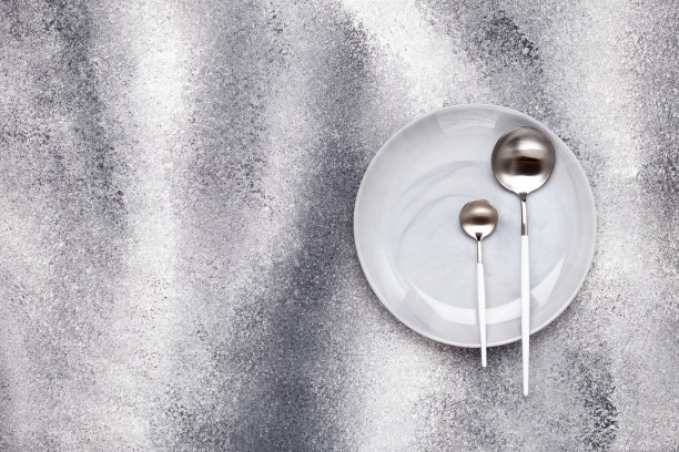 用大汤匙把干净的陶瓷盘子和没有用过的茶匙倒掉。餐具放在灰色的邋遢桌子上，服务理念。单色设计菜单。贺卡，布局，模型与空间。俯视图图片下载