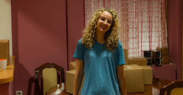 一个漂亮的卷发年轻女人搬进她的新公寓，打开盒子，安排她的衣服和盘子的库存照片。图片下载