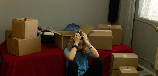 一个漂亮的卷发年轻女人搬进她的新公寓，打开盒子，安排她的衣服和盘子的库存照片。图片下载