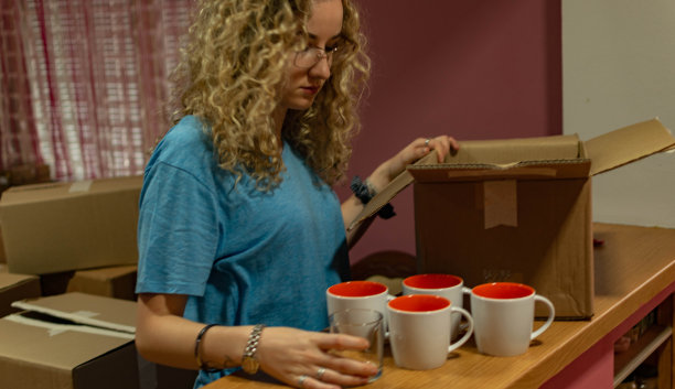 一个漂亮的卷发年轻女人搬进她的新公寓，打开盒子，安排她的衣服和盘子的库存照片。图片下载