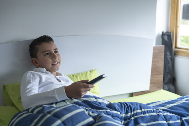 拉丁裔男孩在床上看电视图片下载