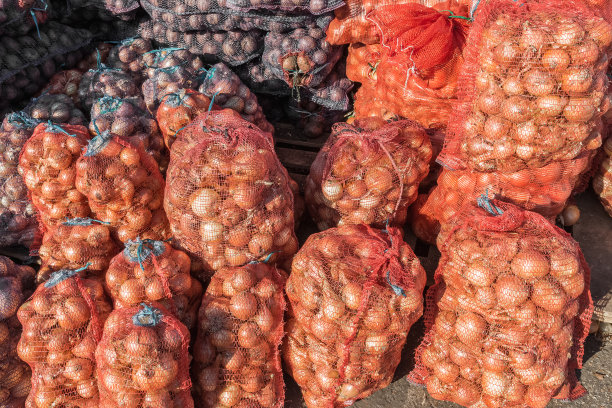 新鲜的蔬菜熟洋葱和土豆装在网里在蔬菜市场出售。图片下载