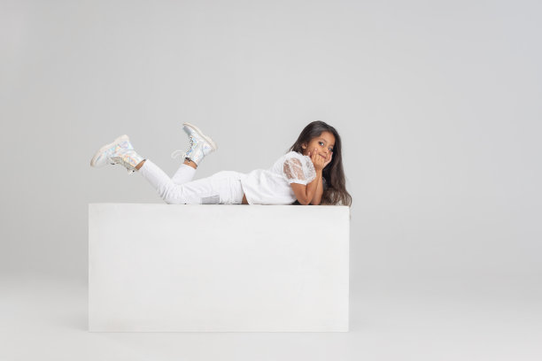 一个可爱的白人小女孩的肖像躺在白色的大盒子上，在白色的工作室背景上。侧面图片图片下载