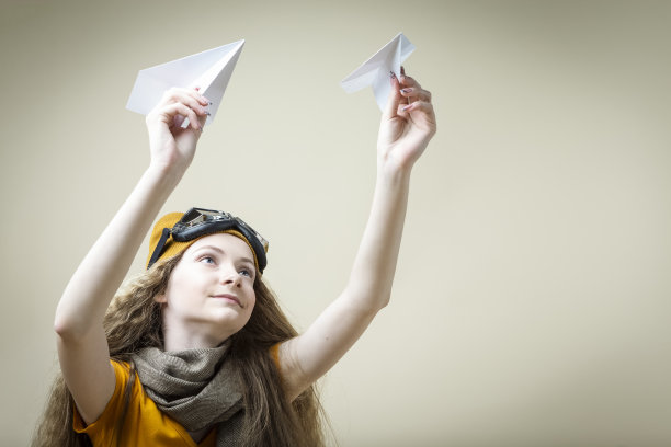 白人金发少女的肖像在飞行眼镜持有两个折纸飞机，而坐在米色背景。水平图像组成图片下载