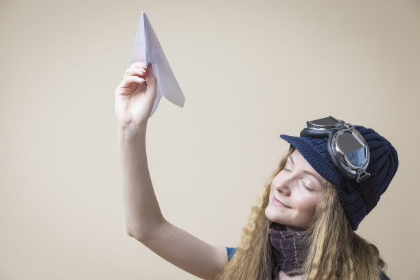 梦想白人少女在飞行眼镜发射折纸飞机在米色背景。水平的形象图片下载