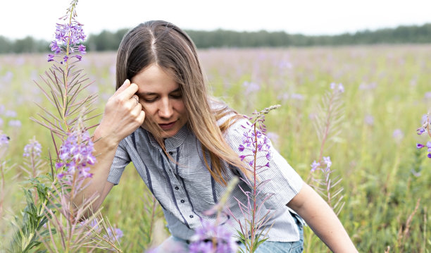 从后面走出来的是一个穿着紫色衬衫、面带微笑的金发美女，她正在草地上的杂草丛中散步图片下载