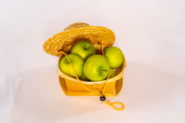 近距离的绿色苹果在篮子上的白色背景。小草帽覆盖着收获的成熟果实。农业和有机食品的概念图片下载
