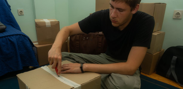 一名学生搬到他的宿舍，拿着装着他的东西的纸箱，坐着或站着把它们放在房间里的库存照片。图片下载
