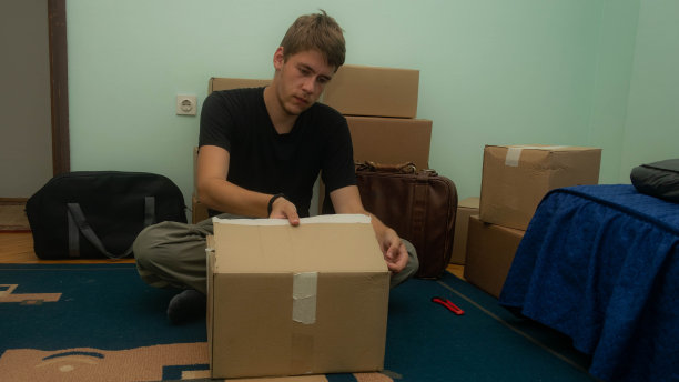 一名学生搬到他的宿舍，拿着装着他的东西的纸箱，坐着或站着把它们放在房间里的库存照片。图片下载