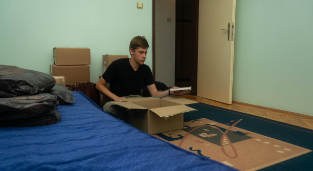一名学生搬到他的宿舍，拿着装着他的东西的纸箱，坐着或站着把它们放在房间里的库存照片。图片下载