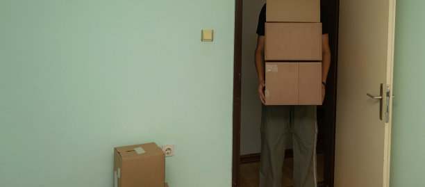 一名学生搬到他的宿舍，拿着装着他的东西的纸箱，坐着或站着把它们放在房间里的库存照片。图片下载