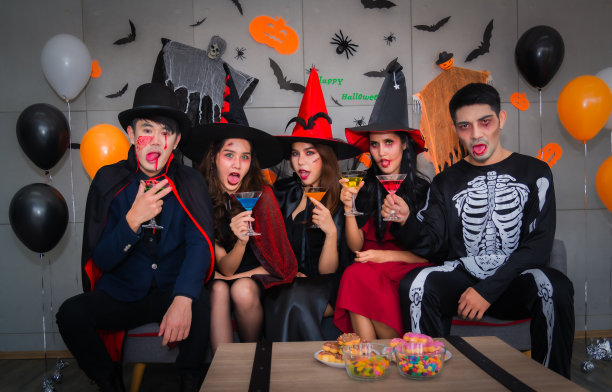 一群快乐的亚洲年轻人在万圣节穿着角色扮演和化妆，坐在沙发上开派对，喝鸡尾酒在夜店。图片下载