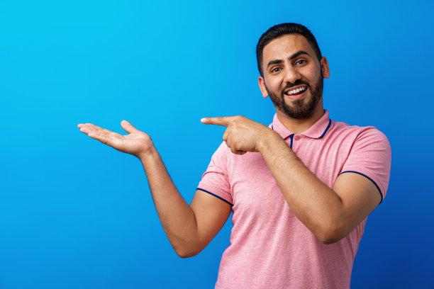 在米色背景上指向空白处并微笑的年轻英俊的阿拉伯男人图片下载