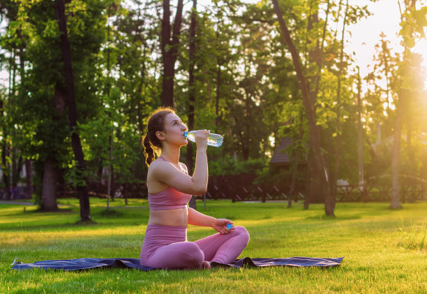日落时分，小女孩在公园里做瑜伽的时候喝水。图片下载
