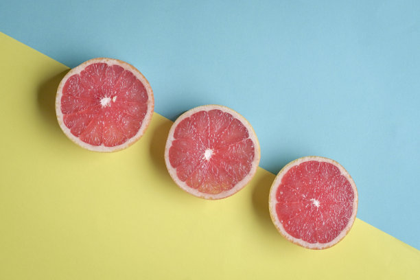 三个熟透的柚子在蓝色和黄色的背景上排成一条线。图片下载