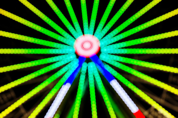 游乐园晚上的图像散焦和模糊。夜景下的摩天轮和云霄飞车。公园骑图片下载