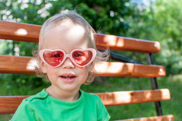 夏天，一个穿着绿色t恤，戴着粉色心形太阳镜的小女孩在公园里散步图片下载