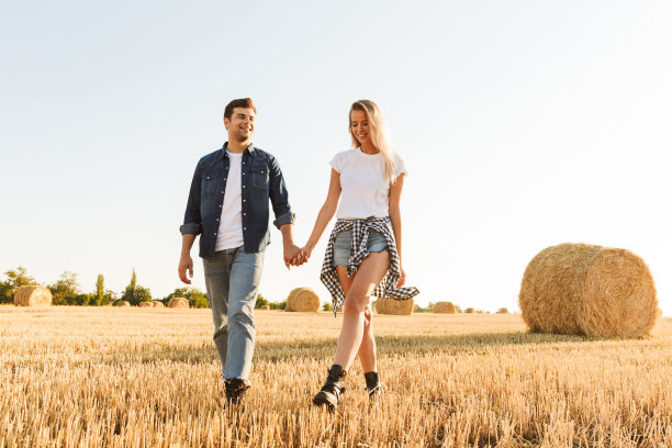 这是一对年轻的男女在阳光明媚的日子里走过金色的田野，和一堆干草堆的照片图片下载